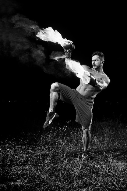 Monochroom shot van een shirtless gespierde sterke jonge mannelijke bokser die buiten oefent met zijn bokshandschoenen vlammend met vuur brandende brandende vurige kracht vertrouwen martial combat fit spieren zweet behendig.