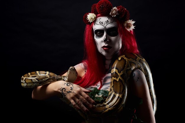 Monstervrouw met tekeningsgezicht en bloemen op hoofd die lange slangenpiton in handen houden