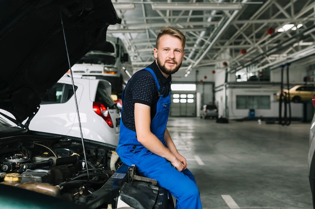 Monteur zittend op auto op workshop