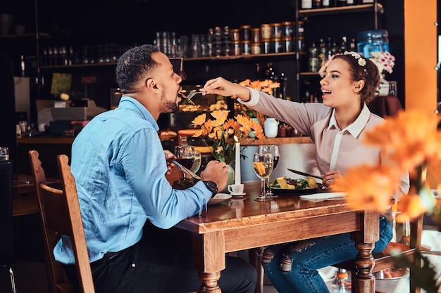 Mooi Afrikaans-Amerikaans verliefd stel dat een geweldige tijd samen heeft tijdens hun dating, een aantrekkelijk stel dat van elkaar geniet, jonge vrouw die haar man voedt in een restaurant.