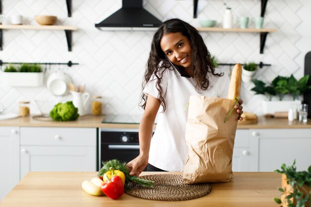 Mooi afro-meisje pakt producten uit een supermarkt uit en praat via de telefoon