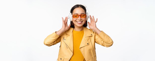 Mooi Aziatisch meisje lachen gelukkig luisteren muziek in koptelefoon staande op witte achtergrond