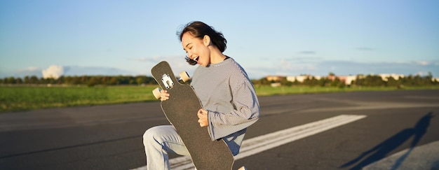 Mooi Aziatisch tienermeisje speelt met haar longboard en houdt skateboard vast alsof ze gitaar speelt