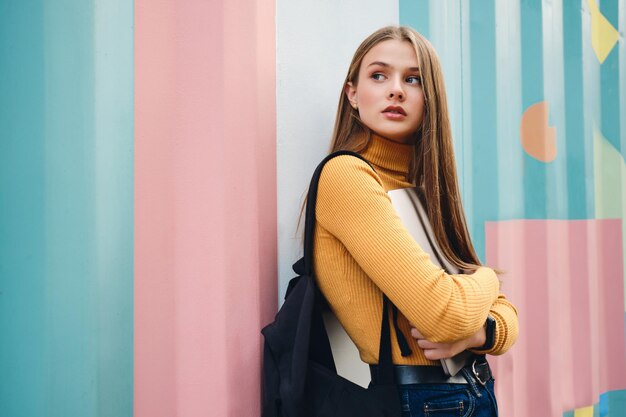 Mooi casual studentenmeisje met laptop die nadenkend wegkijkt over kleurrijke achtergrond buiten