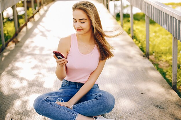 mooi en helder meisje in roze t-shirts en jeans die in het zonnige de zomerpark zitten