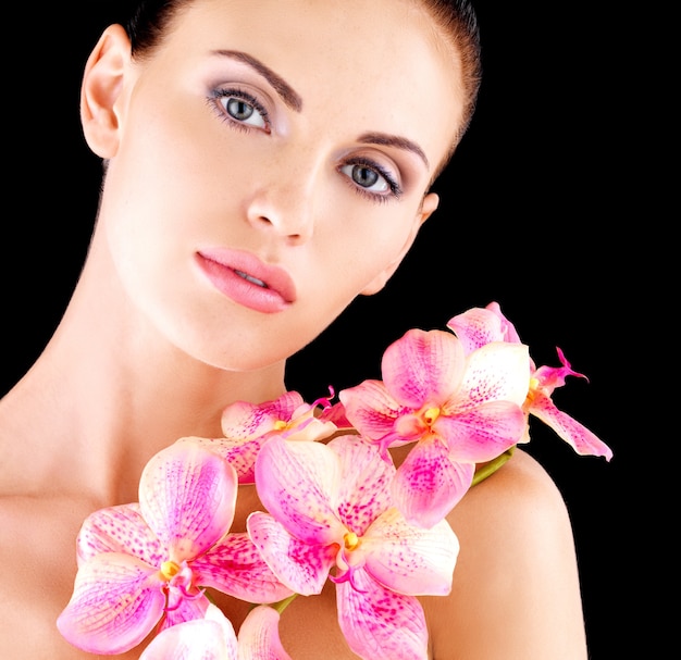 Mooi gezicht van een volwassen vrouw met een gezonde huid en roze bloemen op lichaam - studio