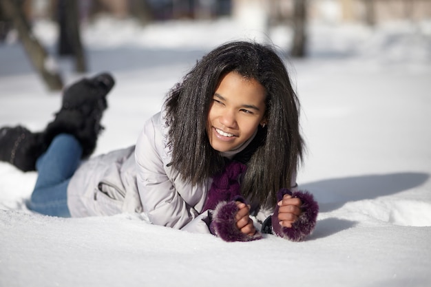 Mooi glimlachend Amerikaans zwart wijfje dat in sneeuw in openlucht ligt