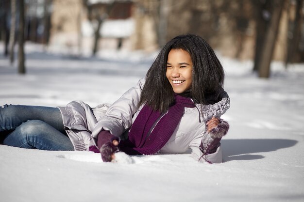 Mooi glimlachend Amerikaans zwart wijfje dat in sneeuw in openlucht ligt