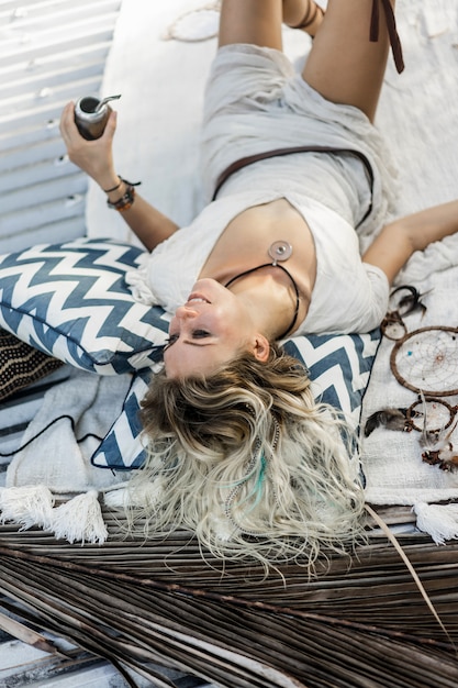 Gratis foto mooi indisch hippiemeisje met lang blond haar op de dak het drinken partnerthee.