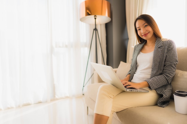 Mooi jong Aziatisch portret die computer en laptop met koffiekopzitting op bank gebruiken