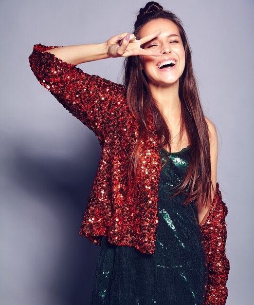 Mooi Kaukasisch het glimlachen hipster donkerbruin vrouwenmodel in heldere shinny wijzend op de zomer modieus jasje en het groene kleding stellen op grijs. Vredesteken tonen