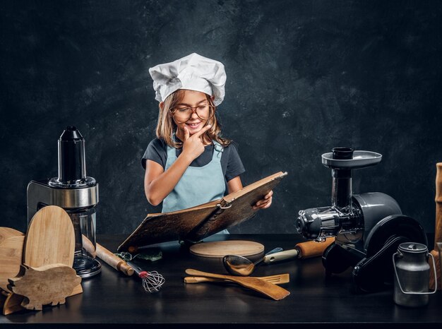 Gratis foto mooi klein meisje leest een receptenboek en heeft een geweldig idee wat ze moet koken voor het avondeten.