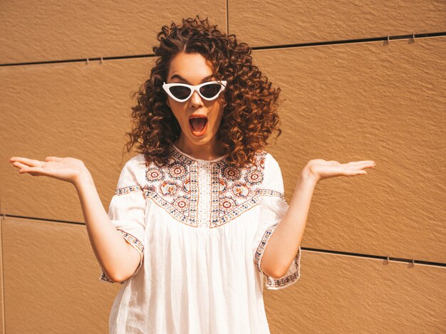 Mooi lachende model met afro krullen kapsel gekleed in zomer hipster witte jurk en zonnebril