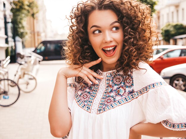 Mooi lachende model met afro krullen kapsel gekleed in zomer hipster witte jurk.