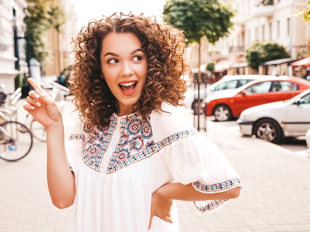 Mooi lachende model met afro krullen kapsel gekleed in zomer hipster witte jurk.