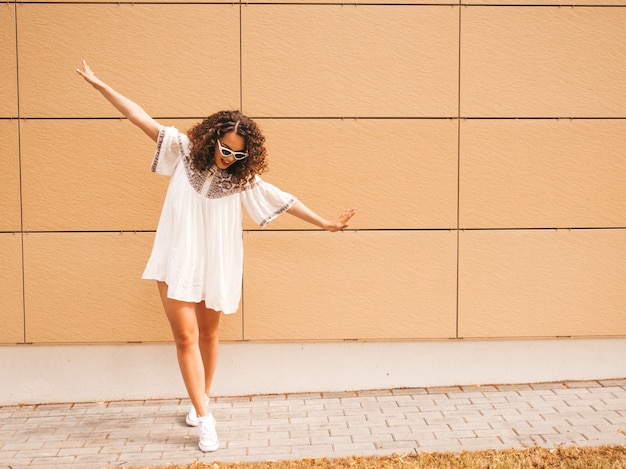 Mooi lachende model met afro krullen kapsel gekleed in zomer hipster witte jurk.