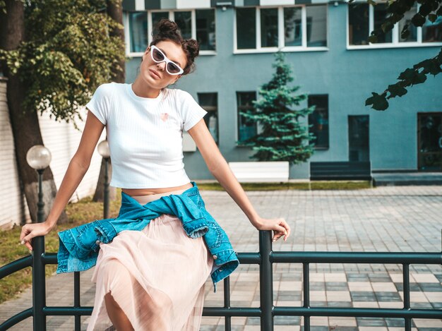 Mooi lachende model met hoorns kapsel gekleed in zomer hipster jas jeans kleding. Sexy zorgeloos meisje poseren in de straat. Trendy grappige en positieve vrouw plezier in zonnebril