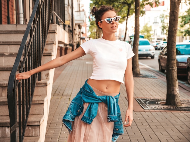 Mooi lachende model met hoorns kapsel gekleed in zomer hipster jas jeans kleding. Sexy zorgeloos meisje poseren in de straat. Trendy grappige en positieve vrouw plezier in zonnebril