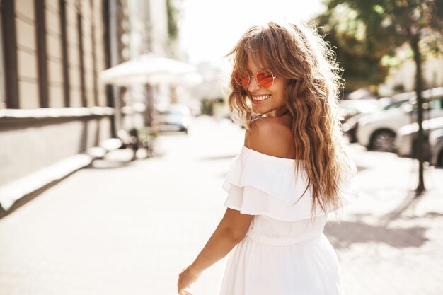 Mooi leuk glimlachend blond tienermodel zonder make-up in de zomer hipster witte kleding die op de straat in zonnebril lopen. Omdraaien