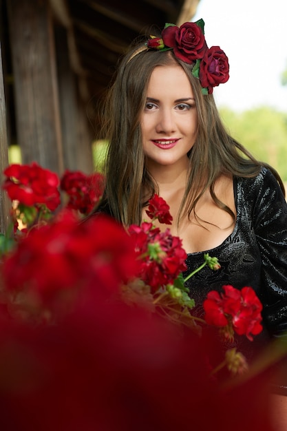 Mooi meisje, brunette in rode bloemkroon, omringd door rode bloemen, portret.