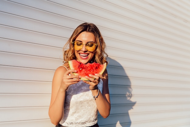 Mooi meisje dat een watermeloen eet, gele zonnebril draagt, die van de de zomerdagen geniet
