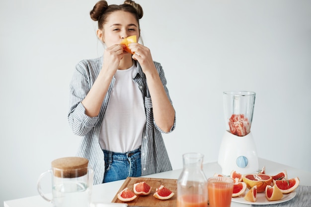 Mooi meisje dat grapefruitstuk over witte muur eet. Gezonde fitnessvoeding. Kopieer ruimte.