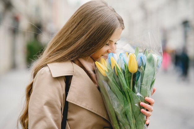 Mooi meisje in een bruine jas. Vrouw in een lentestad. Dame met boeket bloemen