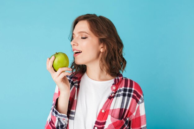 Mooi meisje in geruit overhemd en het eten van groene appel over kleurrijke achtergrond