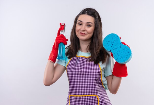 Mooi meisje in schort en rubberen handschoenen met schoonmaak spray en spons camera kijken met blij gezicht lachend