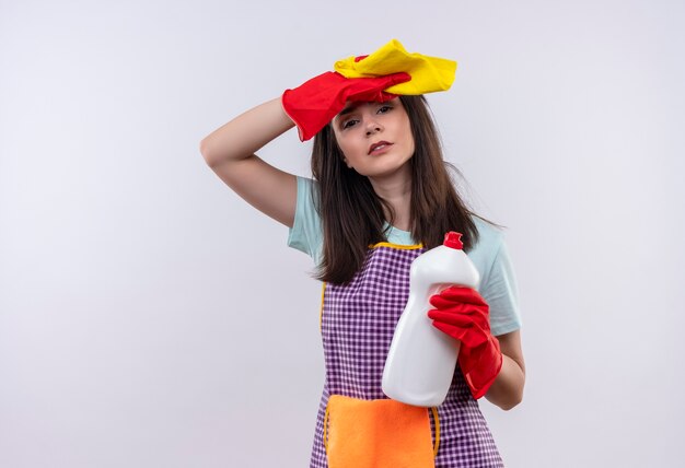 Mooi meisje in schort en rubberen handschoenen met schoonmaakproducten en rud moe en overwerkt hoofd aan te raken