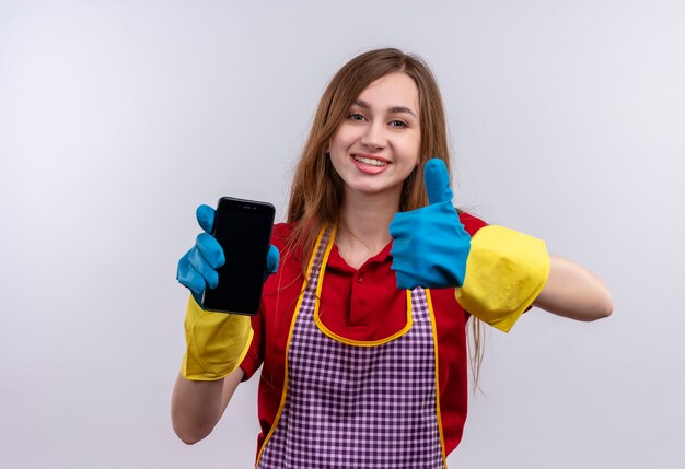 Mooi meisje in schort en rubberen handschoenen met smartphone duimen opdagen glimlachen