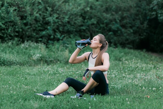 mooi meisje in sport kleding drinkwater na training zittend op het gras