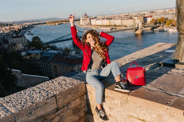 Mooi meisje in trendy rode jas poseren op dak op de achtergrond van de stad