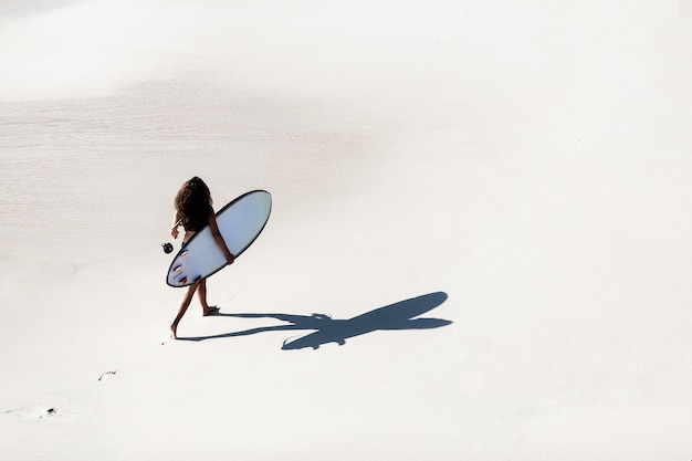 Gratis foto mooi meisje loopt met een surfplank op een wild strand. geweldig uitzicht vanaf de top.