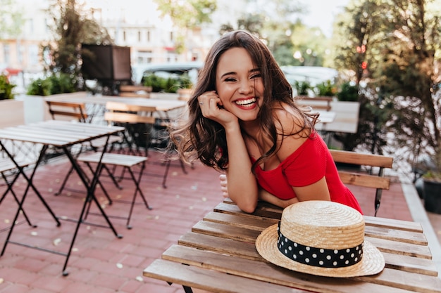 Mooi meisje met donker haar genieten van een goede dag zittend in café. elegante vrouwelijke model tijd doorbrengen in openluchtrestaurant.