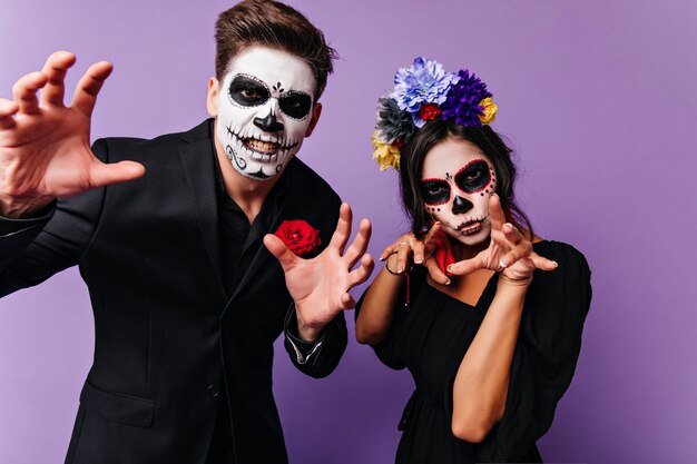 Mooi meisje met enge make-up koelen met vriendje in halloween. Indoor foto van onbezorgd paar met plezier op feestje in vampierkostuums.