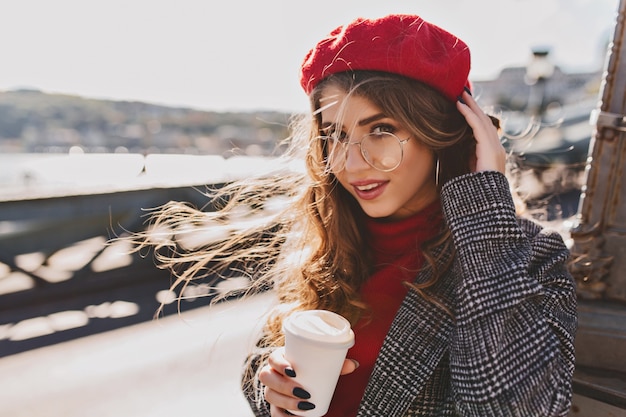 Mooi meisje met grote blauwe ogen poseren op straat in koude winderige dag met kopje koffie