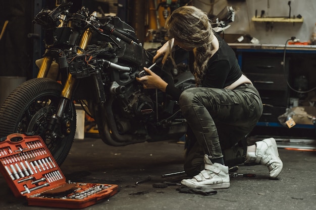 Mooi meisje met lang haar in de garage die een motorfiets herstelt