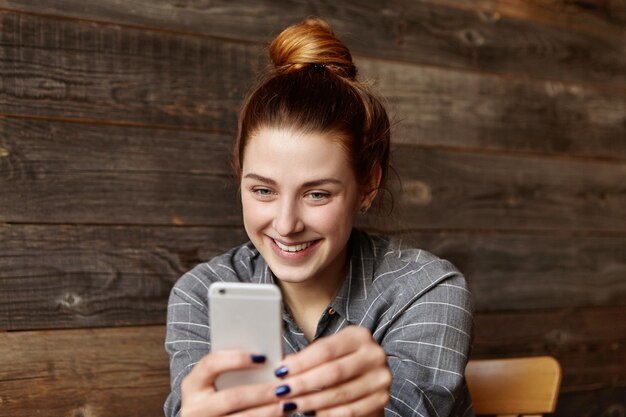 Mooi meisje met mooie charmante glimlach binnenshuis met behulp van slimme telefoon