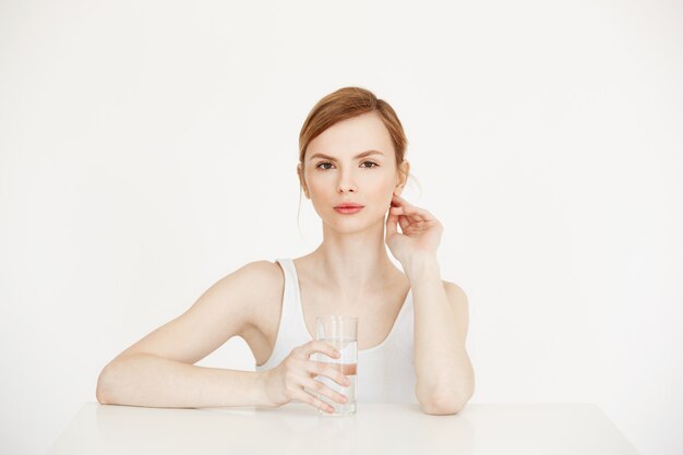 Mooi meisje met schone frisse huid met glas met water zittend aan tafel. Gezondheid en schoonheid levensstijl.