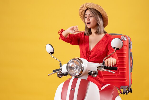 mooi meisje op bromfiets met rode koffer die tijd controleert