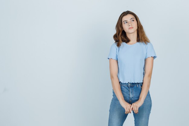 Mooi meisje opzij kijken in t-shirt, spijkerbroek en op zoek doordachte, vooraanzicht.