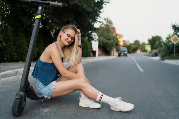 Mooi meisje zit op haar electro-scooter in de zomer op straat