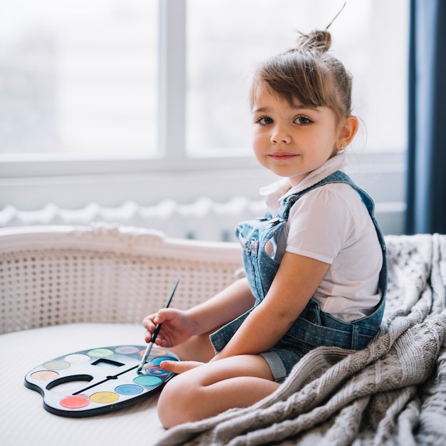 Mooi meisje, zittend op de bank met aquarel palet