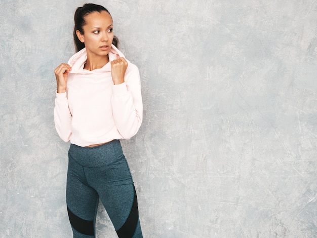 Mooi model met perfect gebruinde lichaam. Vrouwelijke poseren in de studio in de buurt van grijze muur