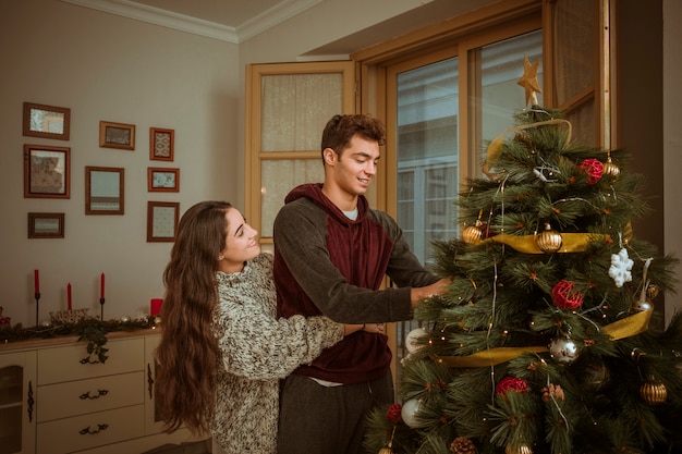 Gratis foto mooi paar die terwijl het verfraaien van kerstboom koesteren