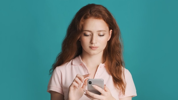 Mooi roodharig meisje dat smartphone op camera over kleurrijke achtergrond gebruikt
