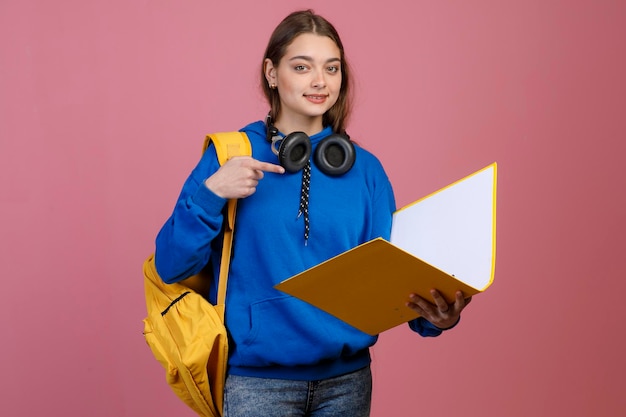 Mooi schoolmeisje dat gele rugzak en map vasthoudt