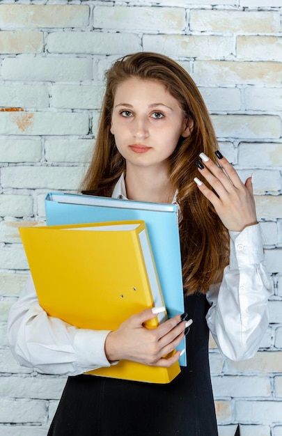 Mooi schoolmeisje in een uniform dat notitieboekjes vasthoudt en naar de camera kijkt