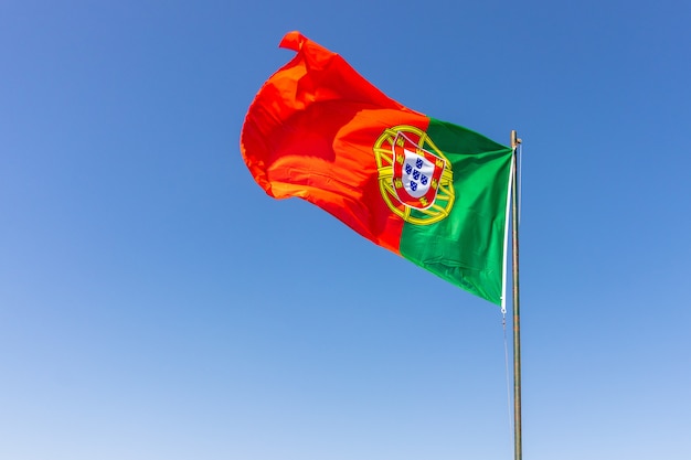 Gratis foto mooi schot van de portugese vlag zwaaien in de kalme heldere hemel